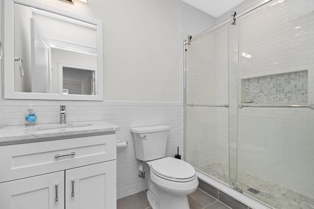 bathroom with vanity, a shower with door, tile patterned floors, toilet, and tile walls