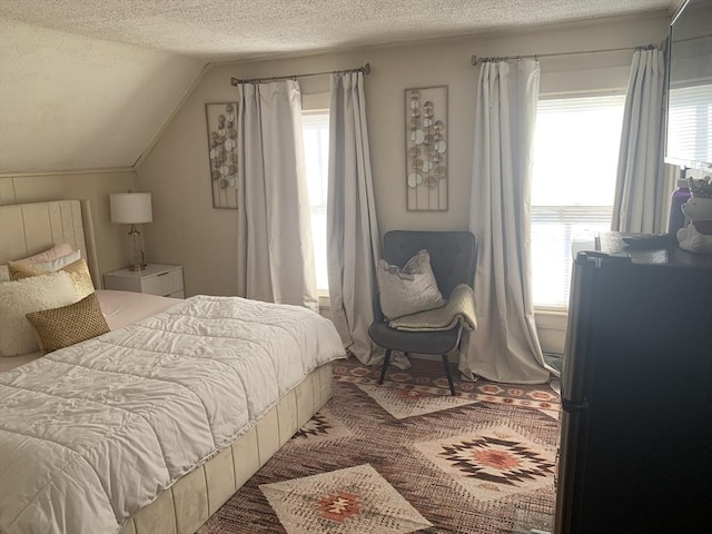 bedroom with vaulted ceiling, stainless steel refrigerator, a textured ceiling, and multiple windows