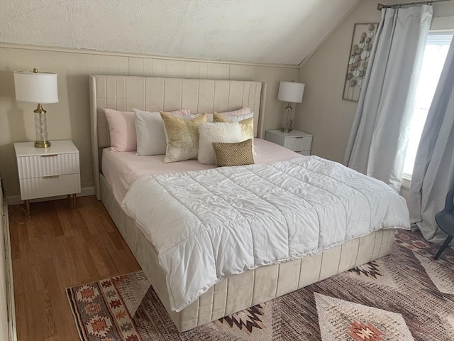 bedroom with light hardwood / wood-style floors, a textured ceiling, and vaulted ceiling