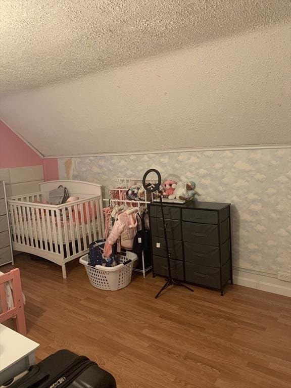 bedroom with a textured ceiling, lofted ceiling, hardwood / wood-style floors, and a crib