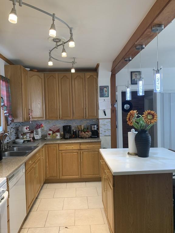 kitchen with white dishwasher, sink, decorative light fixtures, light tile patterned floors, and decorative backsplash