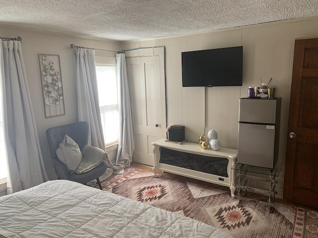 bedroom with a textured ceiling, refrigerator, and wooden walls