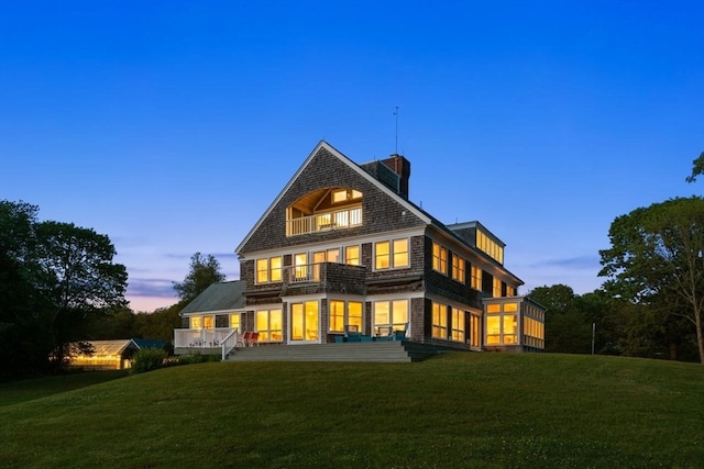 back house at dusk featuring a balcony and a yard