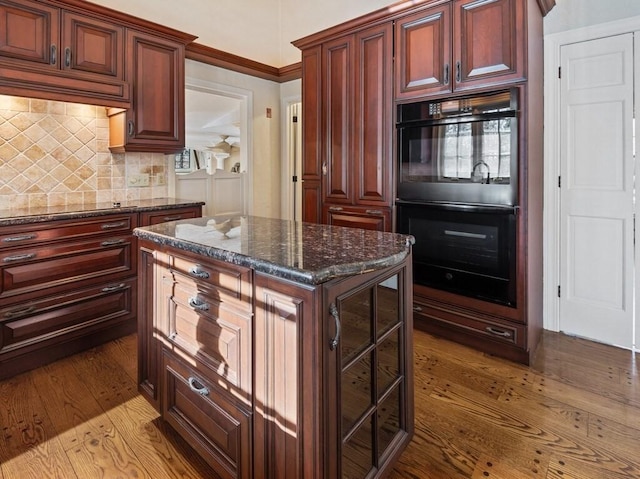 kitchen featuring dark stone countertops, double oven, backsplash, hardwood / wood-style floors, and a center island