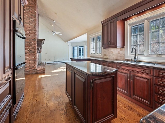 kitchen featuring sink, light hardwood / wood-style flooring, a center island, a baseboard radiator, and vaulted ceiling