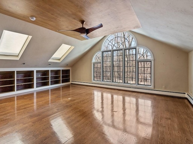 bonus room with a baseboard heating unit, hardwood / wood-style flooring, vaulted ceiling with skylight, and ceiling fan