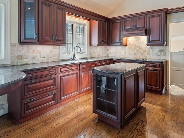 kitchen with sink, vaulted ceiling, dark stone countertops, a kitchen island, and hardwood / wood-style floors