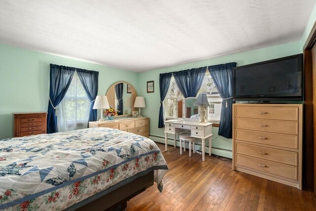 bedroom with multiple windows, hardwood / wood-style floors, and a baseboard radiator