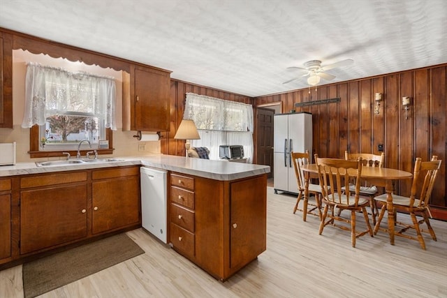kitchen with a peninsula, white appliances, ceiling fan, brown cabinets, and a sink