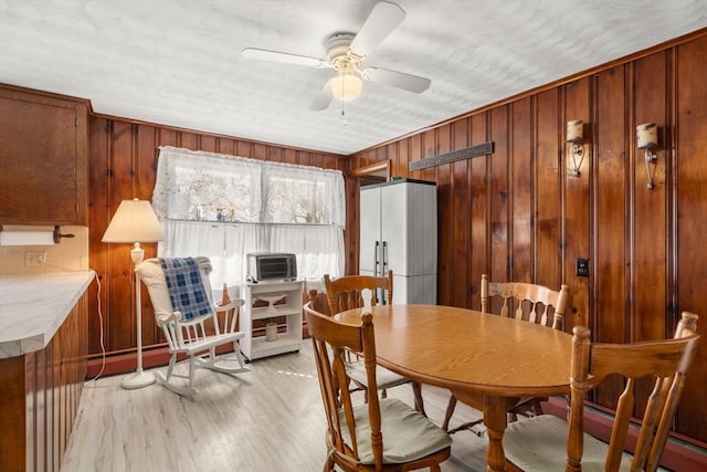 dining area with wooden walls, light wood-style floors, a ceiling fan, and a baseboard heating unit