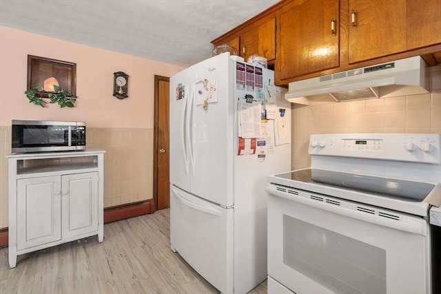 kitchen featuring tile walls, brown cabinets, under cabinet range hood, white appliances, and light wood-style flooring