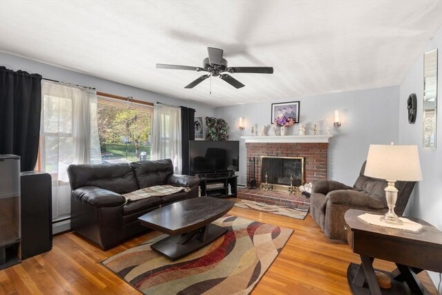 living room with a brick fireplace, ceiling fan, light wood finished floors, and a baseboard radiator
