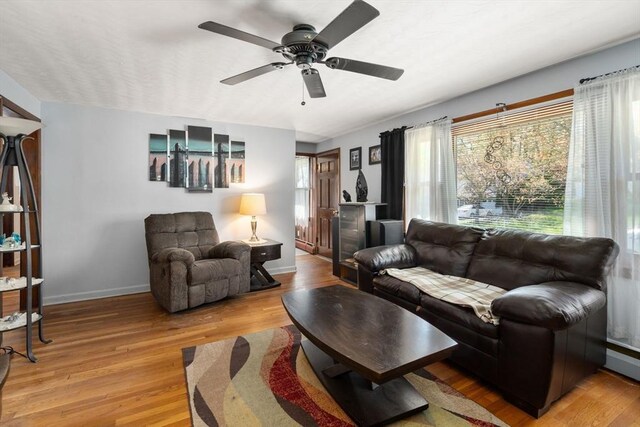 living room with baseboards, light wood-style floors, ceiling fan, and a wealth of natural light