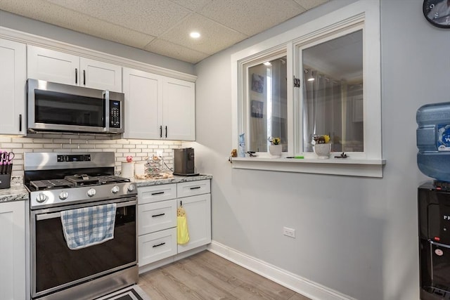 kitchen featuring stainless steel appliances, white cabinetry, baseboards, backsplash, and light wood finished floors