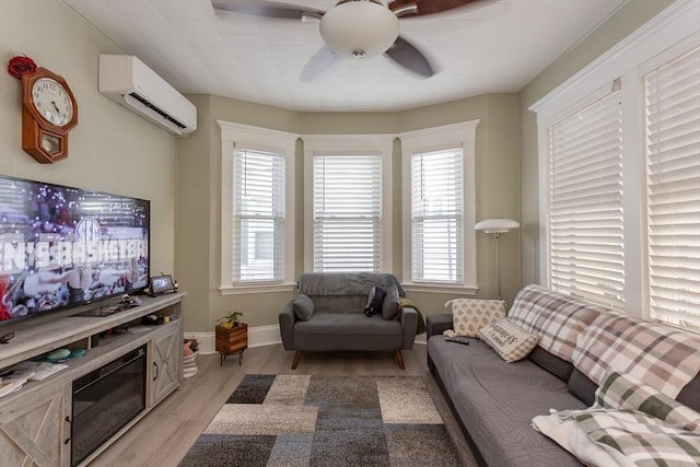 living room featuring ceiling fan, an AC wall unit, light wood-type flooring, and baseboards