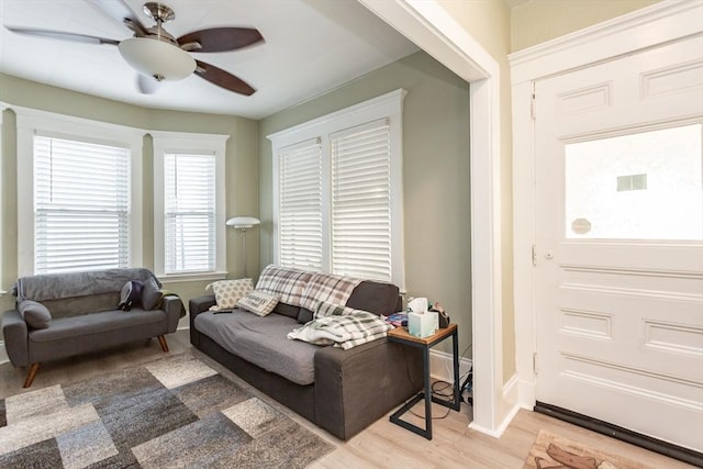 living area featuring a ceiling fan, light wood-type flooring, and baseboards