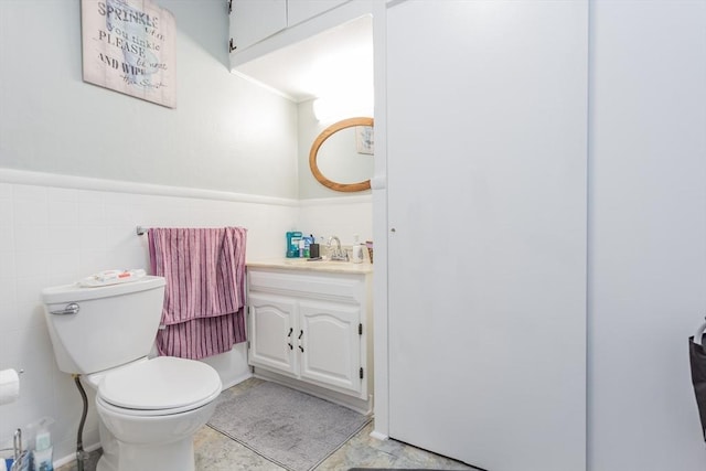 bathroom featuring tile walls, a wainscoted wall, vanity, and toilet