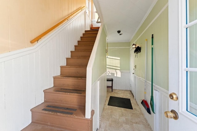 stairway with a decorative wall, wainscoting, and crown molding