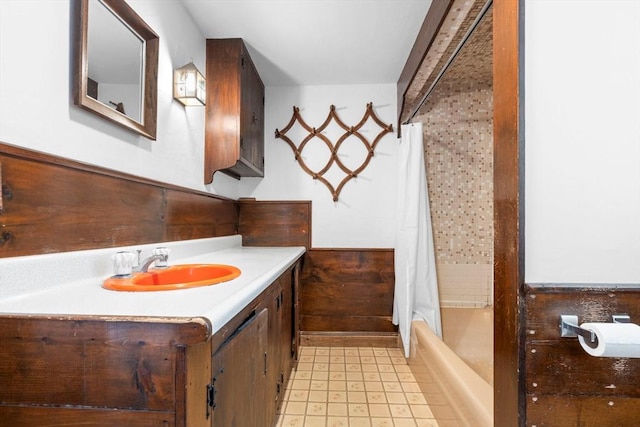 bathroom with vanity, wooden walls, and shower / bath combo with shower curtain