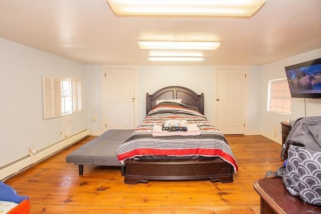 bedroom featuring hardwood / wood-style floors, a baseboard heating unit, and multiple windows