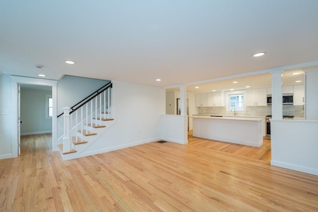 unfurnished living room with recessed lighting, stairway, light wood-type flooring, and baseboards