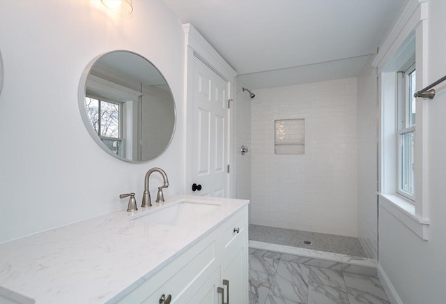 bathroom with marble finish floor, a tile shower, and vanity