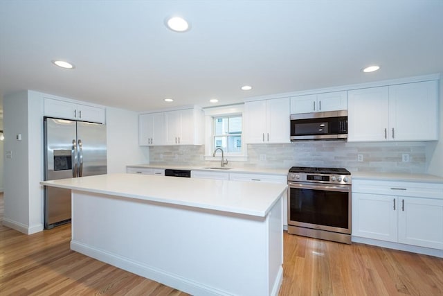 kitchen featuring light wood finished floors, appliances with stainless steel finishes, white cabinets, and a sink