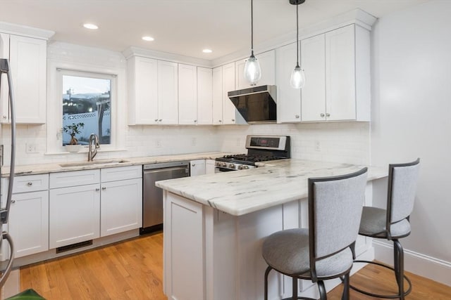 kitchen with exhaust hood, white cabinets, appliances with stainless steel finishes, kitchen peninsula, and a breakfast bar area