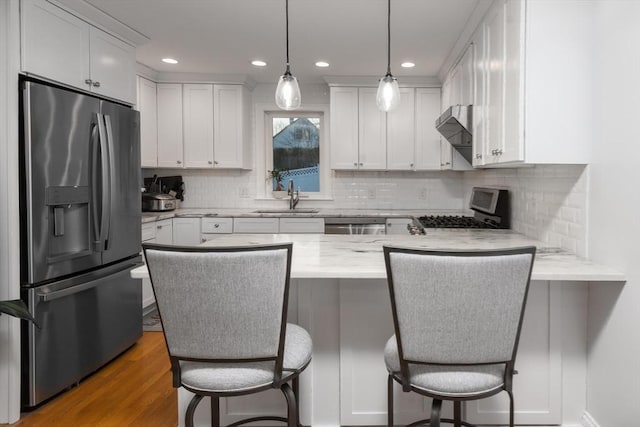 kitchen with light stone countertops, appliances with stainless steel finishes, a breakfast bar, sink, and white cabinets