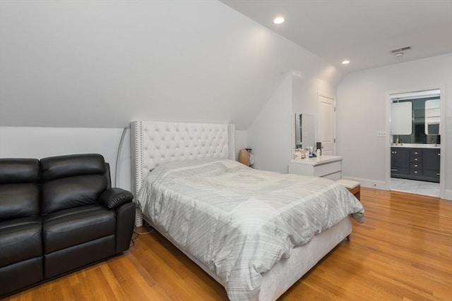 bedroom featuring light wood-type flooring, vaulted ceiling, and ensuite bath