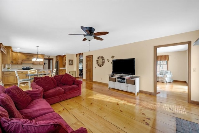 living room with light wood-type flooring and ceiling fan with notable chandelier