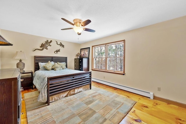 bedroom with ceiling fan, a baseboard heating unit, and light hardwood / wood-style floors