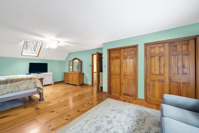 bedroom with light wood-type flooring, vaulted ceiling with skylight, two closets, and ceiling fan