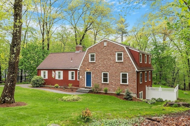 colonial inspired home with a chimney, a gambrel roof, roof with shingles, and brick siding