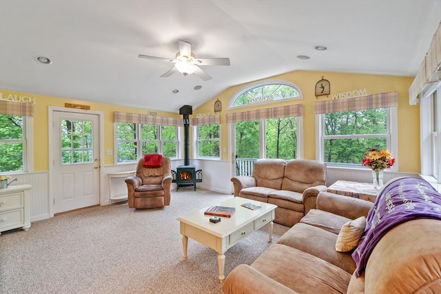 carpeted living room featuring lofted ceiling, a wood stove, and a ceiling fan