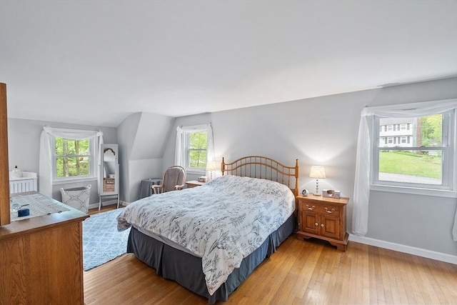 bedroom with light wood finished floors, multiple windows, baseboards, and vaulted ceiling