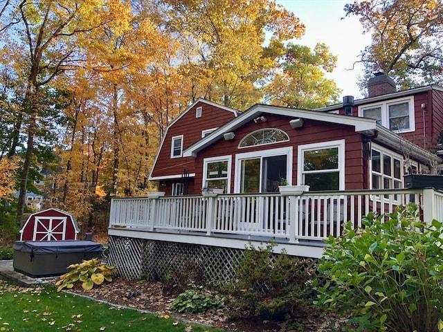rear view of house featuring a wooden deck, a chimney, and a hot tub
