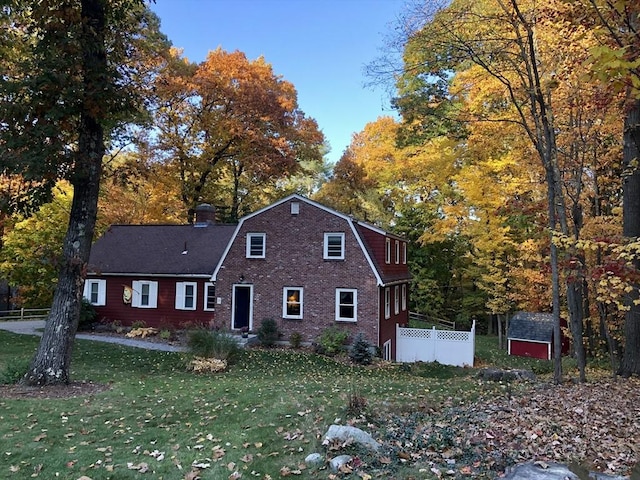 colonial inspired home with a gambrel roof, a storage unit, a chimney, and an outbuilding