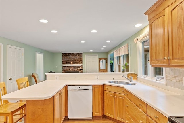 kitchen featuring white dishwasher, a sink, a breakfast bar area, recessed lighting, and light countertops