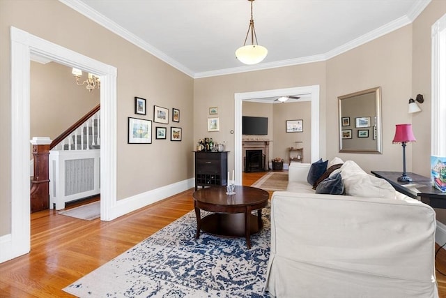 living room with crown molding, a fireplace, baseboards, stairway, and light wood-style flooring