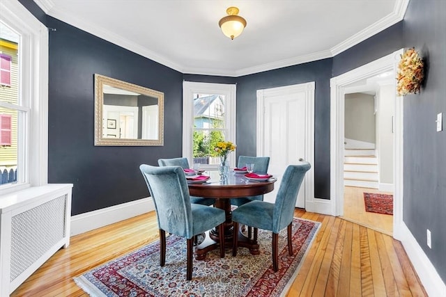 dining room featuring crown molding, light wood-style flooring, radiator, baseboards, and stairway