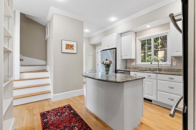 kitchen with ornamental molding, stainless steel refrigerator, dark stone counters, white cabinetry, and a sink