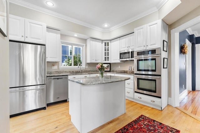 kitchen with light stone countertops, a sink, light wood finished floors, glass insert cabinets, and stainless steel appliances