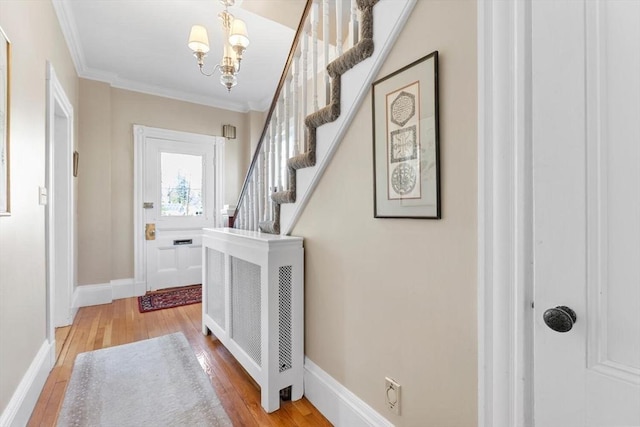 foyer entrance with crown molding, a chandelier, stairs, baseboards, and hardwood / wood-style flooring
