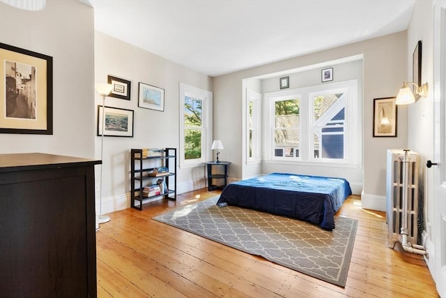 bedroom with radiator heating unit, baseboards, and light wood finished floors