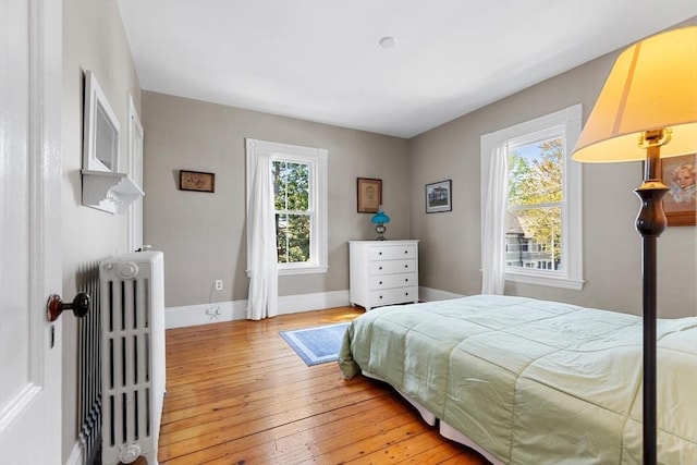 bedroom featuring baseboards, multiple windows, radiator, and light wood-style floors