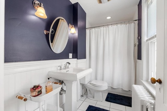 bathroom with wainscoting, toilet, tile patterned floors, shower / bath combo with shower curtain, and radiator heating unit
