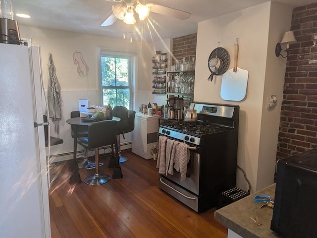 kitchen featuring dark hardwood / wood-style flooring, ceiling fan, stainless steel gas range, brick wall, and white refrigerator