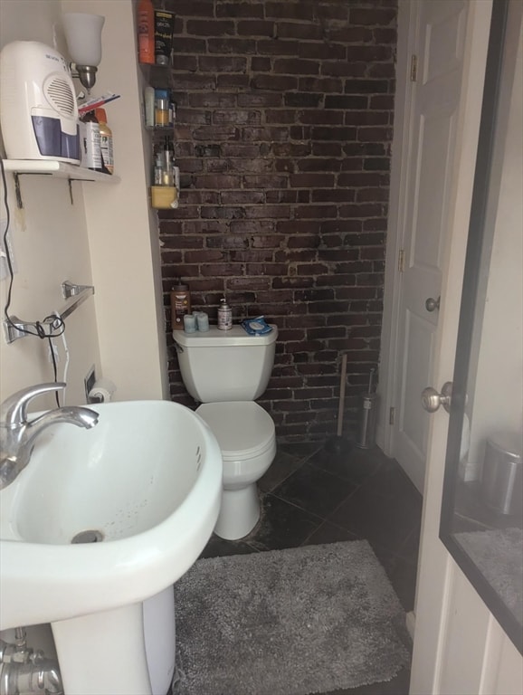 bathroom with toilet, brick wall, tile patterned floors, and sink