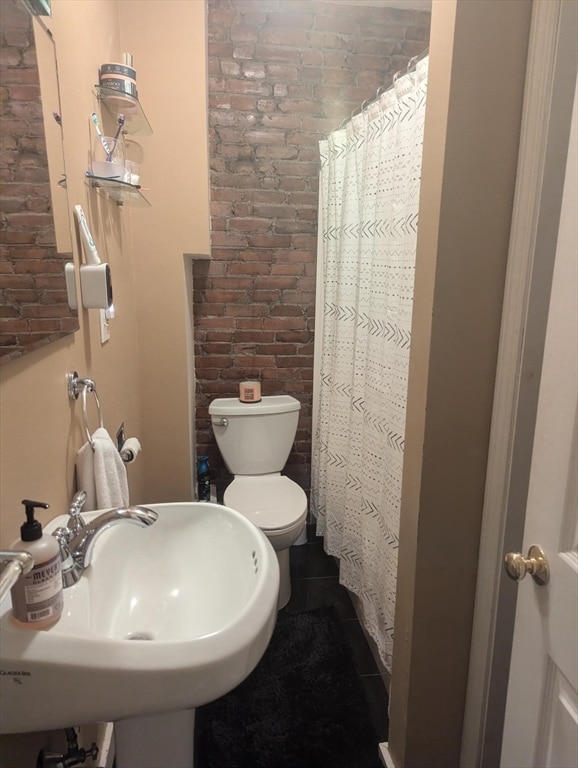 bathroom featuring toilet, brick wall, walk in shower, and sink